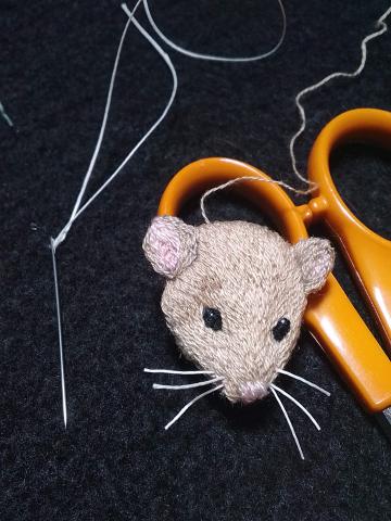 The head of a light brown mouse, about the length of a needle.