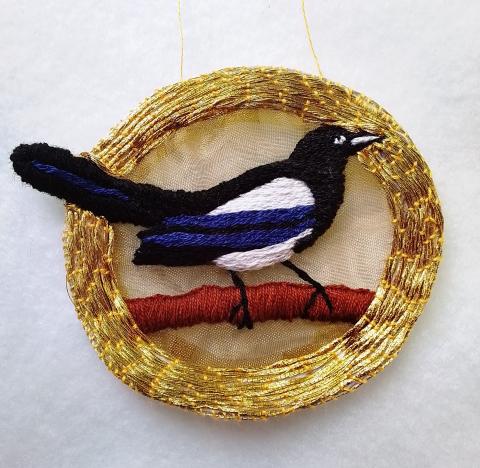An embroidered magpie in a gold circle