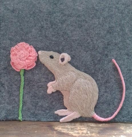 A grey rat is smelling a pink flower. Both are raised off the page.