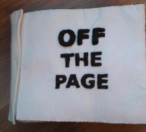 A white cover with black block capitals made from stuffed needlelace that raises all the letters high off the background.