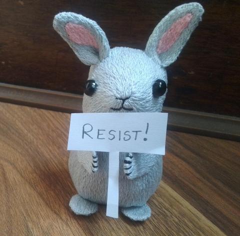 A light-grey stylised rabbit holds up a paper sign saying "RESIST!"
