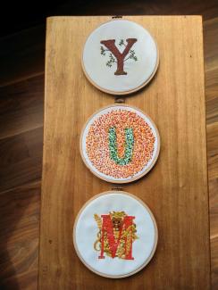 Three small pieces of embroidery, each in a separate embroidery hoop. There's a Y which looks like a tree, with moss at the base of the trunk and small leaves on some small branches; there's a U which is based on a colour-blindness test, so it's made up of green and orange/red dots; there's a red M with a roughly life-sized harvest mouse nesting above it.