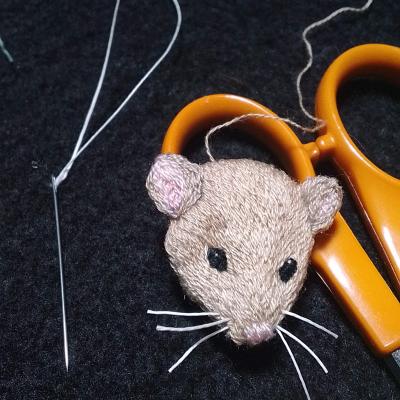 The head of a light brown mouse, about the length of a needle.