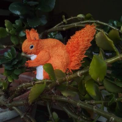 An embroidered red squirrel is sitting on one of my pot plants